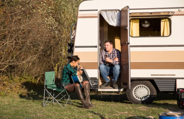 Deux personnes près d'une caravane, l'une joue de la guitare.
