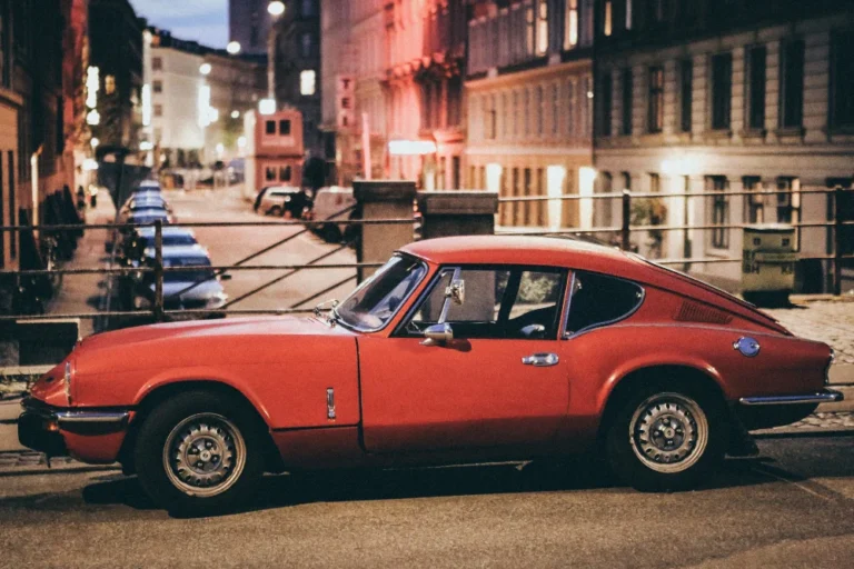 Voiture classique rouge garée dans une rue urbaine éclairée.
