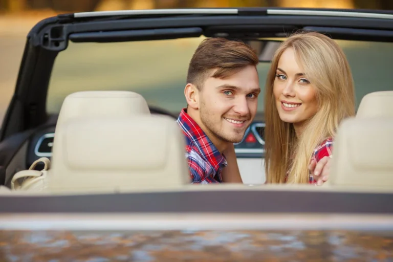 Un couple souriant dans une décapotable, portant des chemises à carreaux.