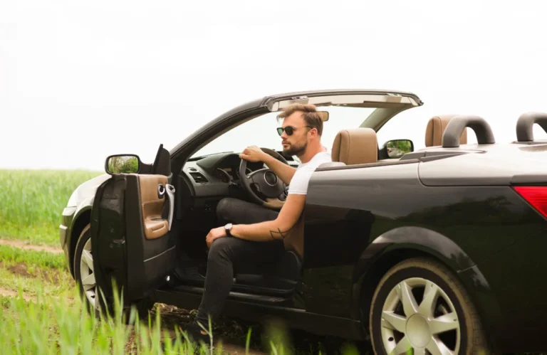 Un homme assis dans un cabriolet noir dans un champ.