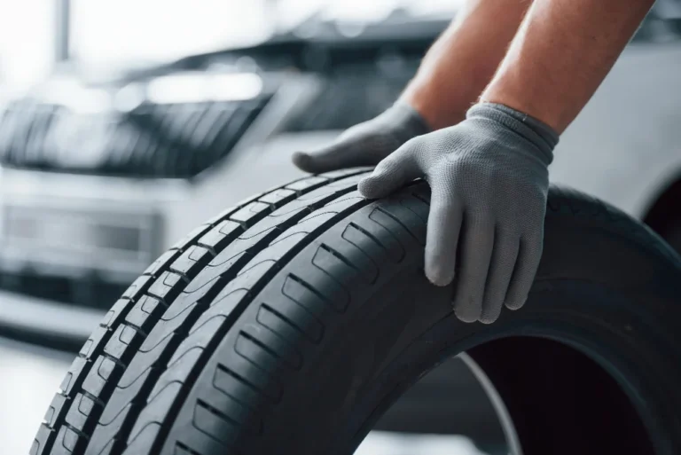 Mains gantées manipulant un pneu devant une voiture floue.