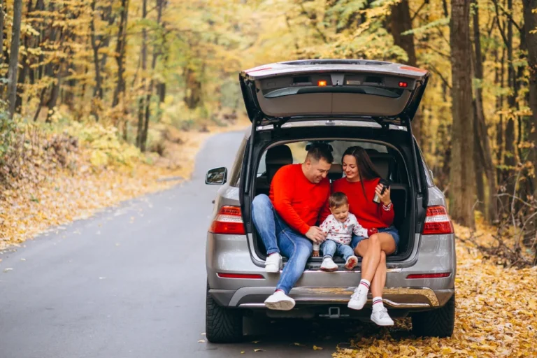 Famille assise dans le coffre d'une voiture sur une route forestière en automne.