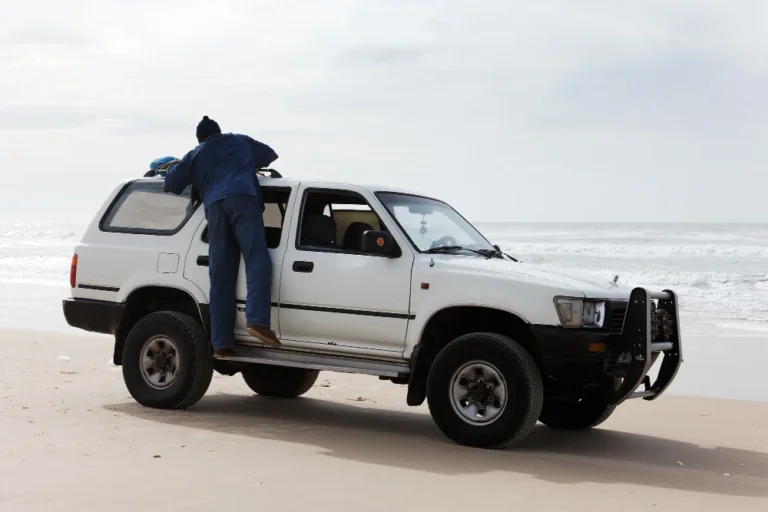 Un homme charge un 4x4 blanc sur une plage.
