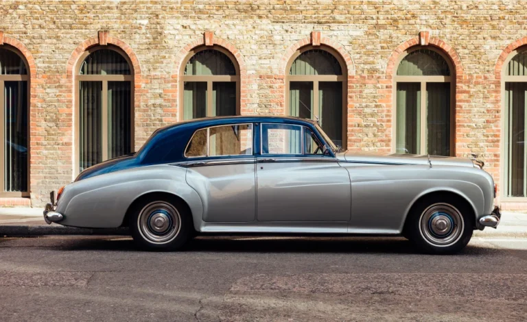 Voiture classique argentée garée devant un mur de briques.