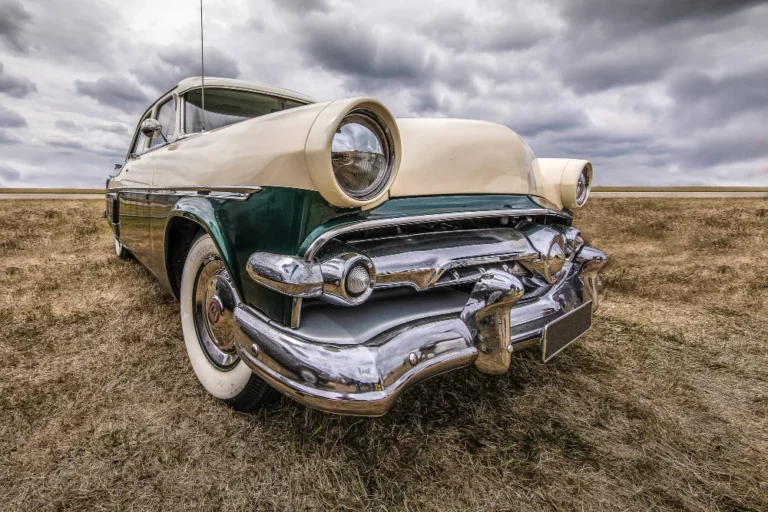 Voiture ancienne sur champ sec sous ciel nuageux.