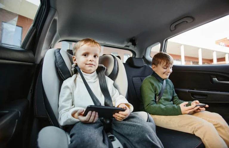 Deux enfants assis à l'arrière d'une voiture, jouant avec des appareils électroniques.