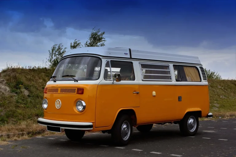 Combi Volkswagen orange garé sur une route, ciel nuageux en arrière-plan.