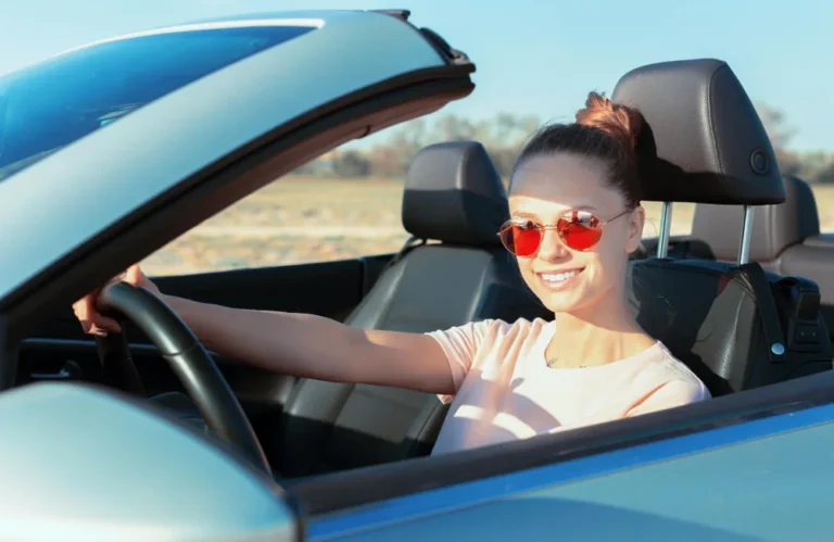 Femme souriante conduisant un cabriolet par une journée ensoleillée.