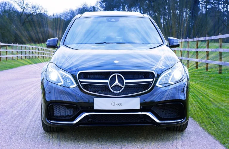 Voiture noire de luxe avec phares allumés sur route de campagne.