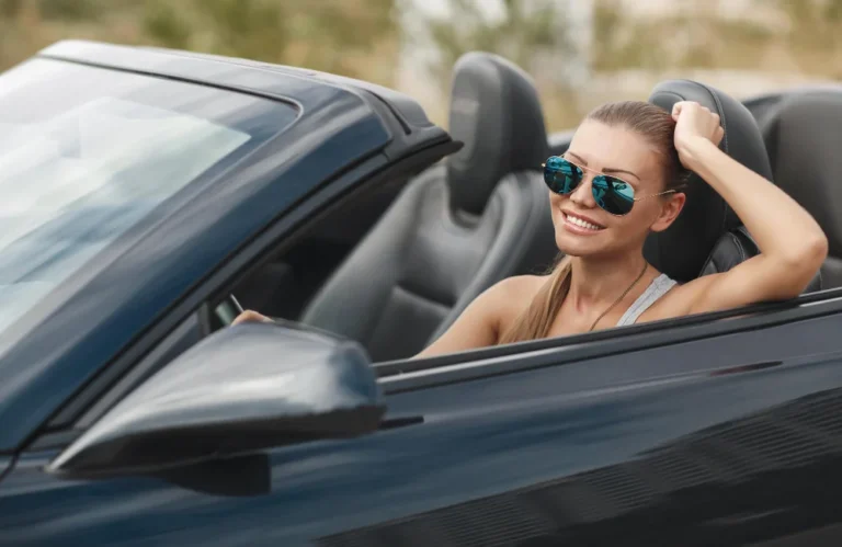 Une femme souriante en lunettes de soleil conduit une décapotable.
